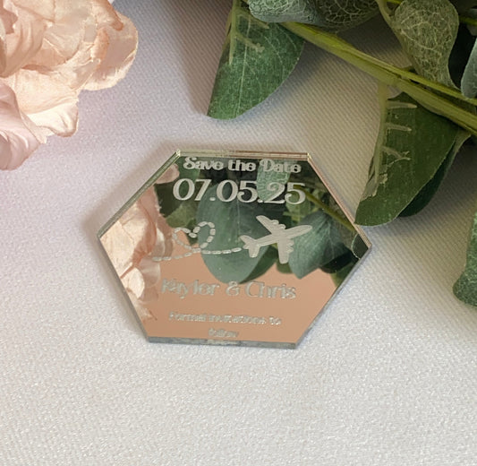 A hexagonal Destination Wedding Save The Date Magnet in mirror silver.The save the date has the wedding date and an aeroplane with a heart shaped trail behind engraved in to the acrylic.