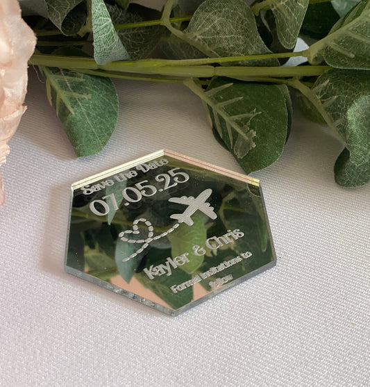 A hexagonal Destination Wedding Save The Date Magnet in mirror silver.The save the date has the wedding date and an aeroplane with a heart shaped trail behind engraved in to the acrylic.