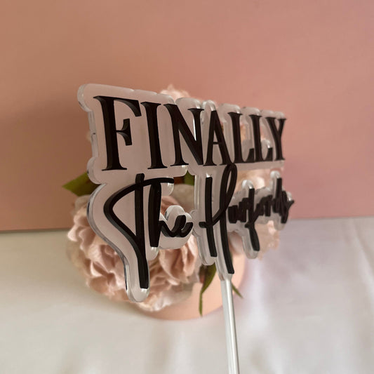 An angled view of a Wedding cake topper made with 2 layers of acrylic with the wording Finally the and the couples surname.