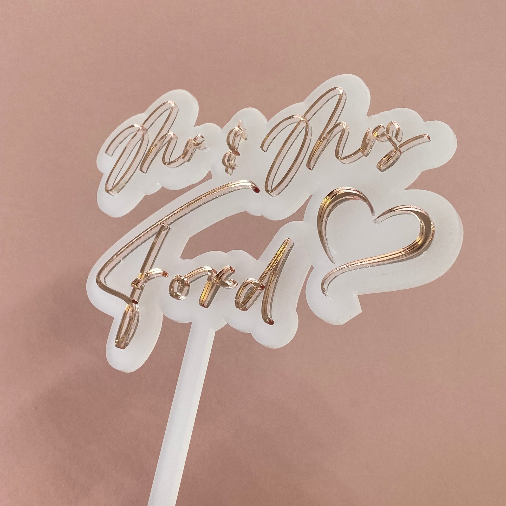 Decorative wedding cake topper with rose gold text on a frosted white acrylic background